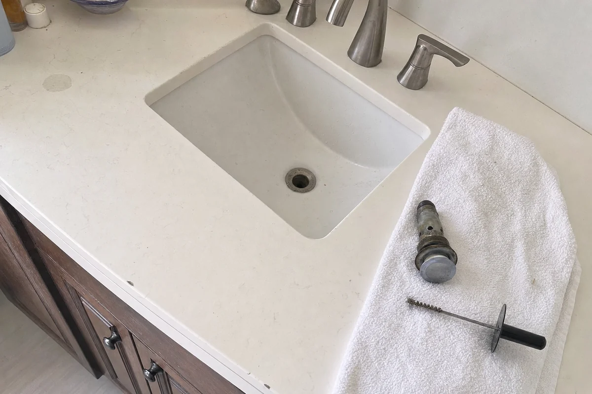 Bathroom sink with the pop-up stopper out and a hand drain snake on a towel
